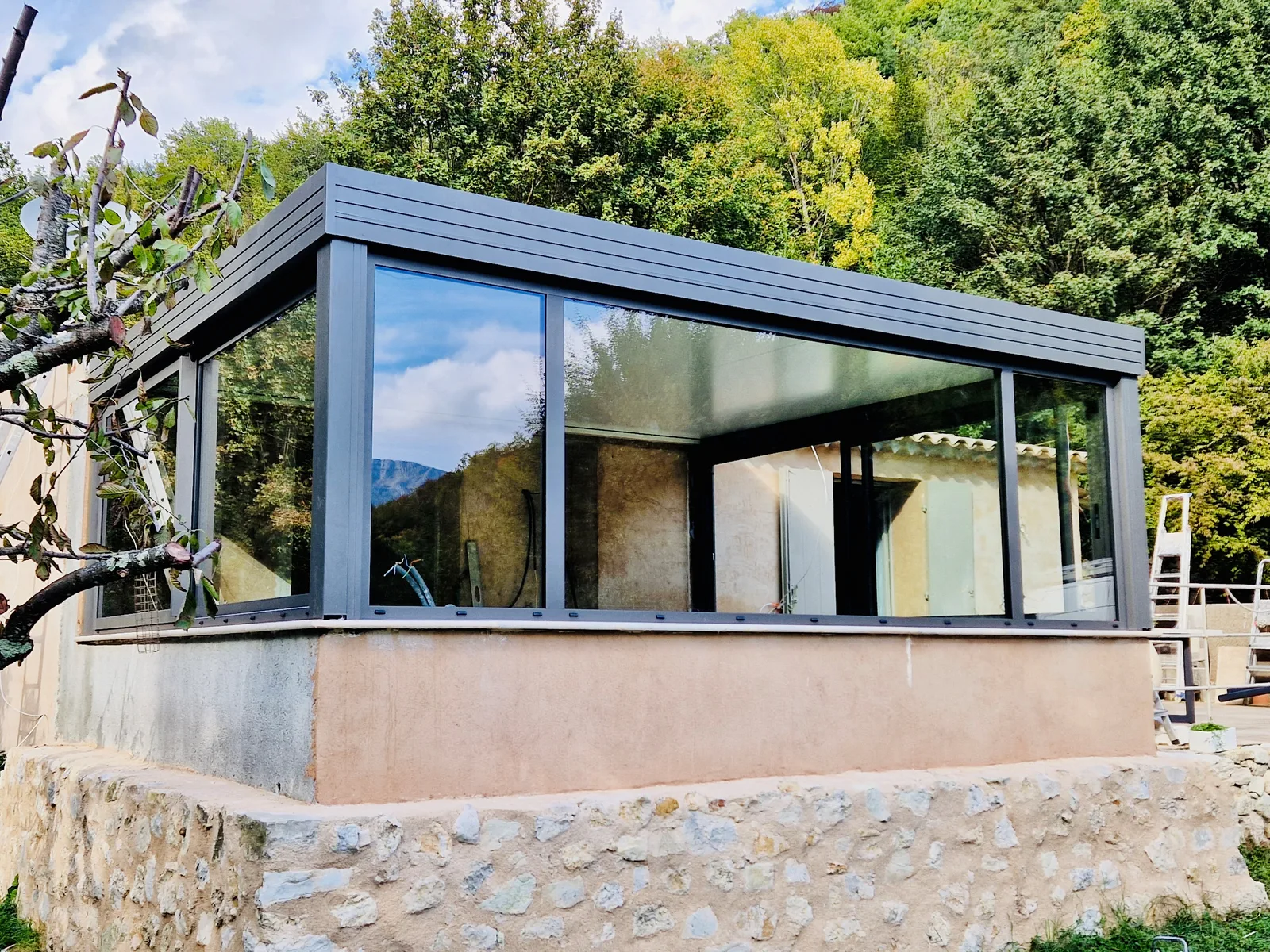 Véranda aluminium et verre intégrée dans son environnement boisé, illustrant l'engagement Art & Fermetures pour des chantiers respectueux du paysage local
